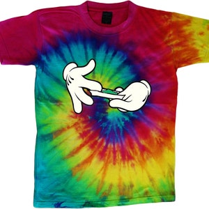 May include: A tie-dye t-shirt featuring a cartoon hand holding a rolled-up green object. The shirt has a rainbow swirl pattern.
