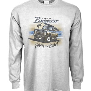 Może przedstawiać: Szary t-shirt z długim rękawem z grafiką w stylu vintage przedstawiającą Forda Bronco jadącego po plaży z tekstem "Ford Bronco" i "Enjoy the Ride!"