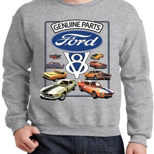 May include: A grey sweatshirt with a graphic of classic Ford Mustangs. The design includes the Ford logo, the words "GENUINE PARTS", and a "V8" emblem. Various vintage car illustrations in orange, yellow, and green are also displayed.