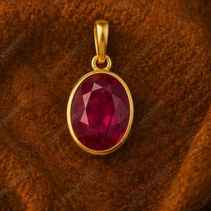 May include: A gold pendant featuring a large, oval-cut, deep red gemstone with a faceted surface. The pendant has a smooth, polished gold bezel setting and a matching gold bail at the top for attachment to a chain, showcasing a classic design.