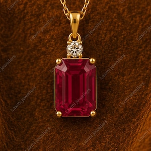Peut inclure: Un pendentif en or avec une grande pierre précieuse rouge foncé de taille émeraude rectangulaire maintenue par quatre griffes. Au-dessus, une pierre plus petite, ronde et transparente est fixée sur une bélière en or avec une chaîne.