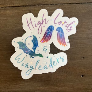 May include: A holographic sticker with a blue and green dragon and a pair of rainbow wings. The text "High Lords & Wingleaders" is written in a cursive font.