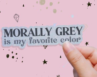May include: A sticker with the text "MORALLY GREY is my favorite color" in a dark grey font. The sticker has a light blue border and is held against a pink background with star and diamond illustrations.