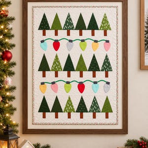 Può includere: Una trapunta da parete rettangolare con tre file orizzontali di alberi di Natale in tessuto verde con tronchi marroni, separate da due file di lampadine natalizie in tessuto colorato su un filo verde, su sfondo bianco.