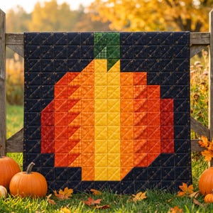 May include: A square quilt featuring a pixelated pumpkin design in shades of yellow, orange, and red, set against a dark navy blue background with a subtle gold star pattern and a green fabric stem at the top center.