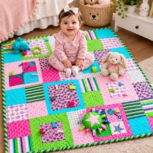 May include: A rectangular baby activity quilt featuring a patchwork design of bright pink, turquoise, and lime green squares with various patterns, including polka dots, stripes, and star motifs, accented with attached fabric loops and toys.