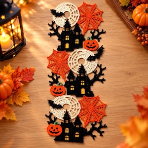May include: A Halloween-themed table runner featuring a repeating pattern of black crocheted haunted houses, orange spider webs, white circular doilies, black bats, and orange jack-o'-lanterns with green stems arranged in a vertical decorative strip.