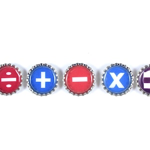 May include: Five bottle caps with different mathematical symbols on them. The symbols are division, addition, subtraction, multiplication, and equals. The caps are red, blue, and purple.