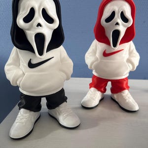 Op de afbeelding: Twee gestileerde figuren met het iconische Ghostface-masker. Eén figuur draagt een zwarte capuchon, een witte hoodie met een zwarte Nike-swoosh en een zwarte broek. De andere draagt een rode capuchon, een witte hoodie met een rode Nike-swoosh en een rode broek.