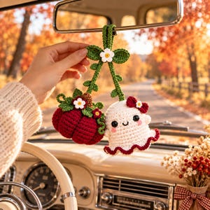 May include: A crochet car hanging ornament featuring a dark red pumpkin and a white ghost with black eyes and a smile. Both are connected by green crocheted stems with small white flowers and green leaves, topped with a green hanging loop.