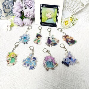 May include: A collection of eight acrylic keychains featuring various anime-style characters in colorful outfits, accompanied by a rectangular card displaying a character illustration with the text STAX 15 ISO 800 F5.6 1/3000.