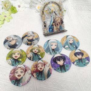 May include: An acrylic standee featuring an anime character in a blue robe and nine circular pin-back buttons displaying various anime characters with names like Qifrey, Coco, Richeh, Agott, and Tetia printed on the colorful, illustrated surfaces.