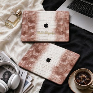 May include: Two laptop covers featuring a brown and white crocodile skin texture pattern. Each cover displays a black Apple logo in the center. One cover includes the gold text "Violet Kingsley" printed below the logo.