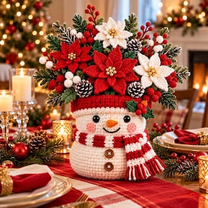 May include: A crocheted snowman centerpiece featuring a white body, a red and white striped scarf, and two brown buttons. The snowman is topped with a festive arrangement of red and white poinsettias, green pine sprigs, red berries, and pinecones.