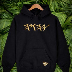 May include: Black hoodie with a gold Hebrew script design and a gold menorah emblem. The hoodie has a front pocket and a hood. The text "www.Custom Designs By Sis Rere.com" is at the top of the image.