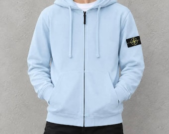 Può includere: Una felpa con cappuccio e zip color azzurro, dotata di coulisse, maniche lunghe e una toppa nera sulla manica sinistra con un logo giallo a forma di bussola. Il capo presenta una chiusura a zip frontale completa e due tasche anteriori.