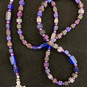 May include: A purple, blue, and gray wooden bead rosary with a silver crucifix and a silver charm.