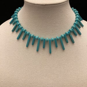 May include: A turquoise blue necklace with round beads and long, thin, rectangular turquoise blue pendants.