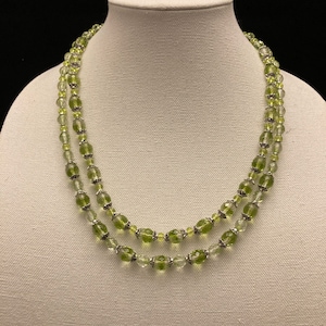 May include: A double strand necklace made with green and clear glass beads. The beads are oval shaped and have a faceted finish.