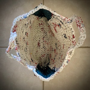 May include: A white crocheted tote bag with red and blue accents. The bag has a blue lining and two handles.