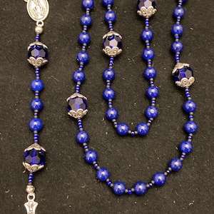 May include: A blue rosary with silver accents and a silver crucifix. The beads are dark blue and the accents are silver. The crucifix is silver and has a figure of Jesus on it.