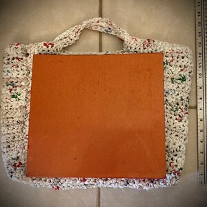 May include: White crocheted tote bag with colorful plastic accents. The bag is empty and has a brown cardboard insert.