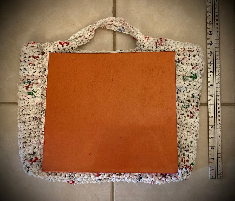 May include: White crocheted tote bag with colorful plastic accents. The bag is empty and has a brown cardboard insert.