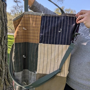 Op de afbeelding: Een patchwork tote bag met een groene canvas band. De tas is gemaakt van verschillende stoffen, waaronder ruit, gestreept en effen kleuren. De tas heeft een bruin, groen en beige kleurenschema.