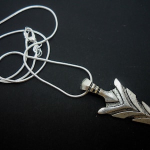 May include: A silver chain necklace with a silver arrowhead pendant. The arrowhead is detailed with intricate lines and has a pointed tip.