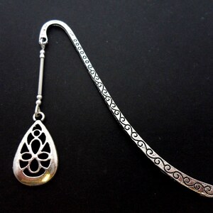 May include: Silver bookmark with a decorative, openwork teardrop design. The bookmark has a long, thin stem with a decorative pattern.