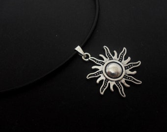 May include: A silver sun pendant necklace on a black cord. The sun has a detailed design with rays and a textured center.