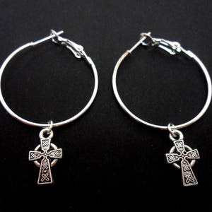 May include: Silver hoop earrings with a Celtic cross charm. The cross is detailed with intricate knotwork.