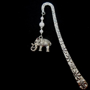 Puede incluir: Marcapáginas de plata con un diseño floral detallado y un dije de elefante de plata que cuelga de cuentas blancas.