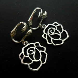 May include: A pair of silver clip-on earrings featuring a rose design. The roses are openwork and have a delicate, feminine look.