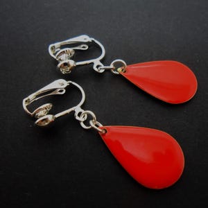 May include: A pair of red teardrop-shaped clip-on earrings with silver-toned metal clasps and connecting chains.