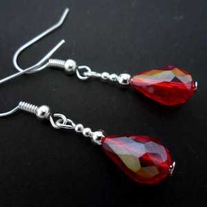 May include: A pair of silver earrings with red teardrop-shaped crystal beads.