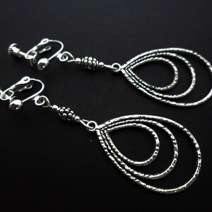 Peut inclure: Une paire de boucles d'oreilles clips argentées avec un design en forme de larme. Les boucles d'oreilles ont trois cercles concentriques qui créent un effet de superposition.