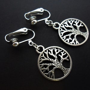 May include: A pair of silver clip-on earrings featuring a tree of life design. The earrings are made of metal and have a circular shape.