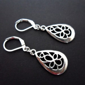 Può includere: Un paio di orecchini pendenti in argento con un design a forma di lacrima. Gli orecchini presentano un delicato motivo traforato, perfetto per aggiungere un tocco di eleganza a qualsiasi outfit.