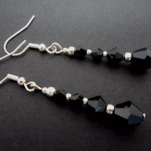 May include: A pair of silver dangle earrings featuring black crystal beads. The earrings have a simple design and are ideal for everyday wear.
