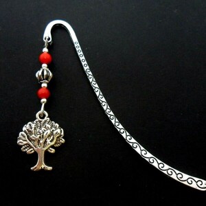 May include: Silver bookmark with a tree charm and red beads. The bookmark has a decorative, swirling design.