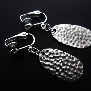Peut inclure: Une paire de boucles d'oreilles clips argentées avec des breloques ovales martelées.