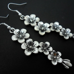May include: A pair of silver dangle earrings with a floral design. Each earring features a chain of five silver flowers.