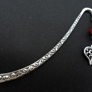 May include: Silver bookmark with a decorative swirl design and a red bead charm with a silver heart pendant.