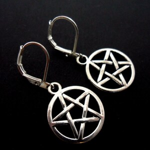 May include: Silver-coloured earrings with a pentagram design inside a circle. The earrings have lever-back clasps and are set against a black backdrop. The pentagram is a five-pointed star.