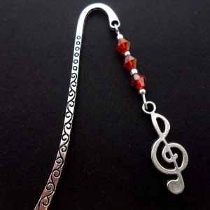 Könnte beinhalten: Silbernes Lesezeichen mit einem Charm in Form eines Violinschlüssels und roten Kristallperlen.