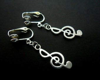 Peut inclure: Une paire de boucles d'oreilles clips argentées avec un charme de clé de sol. Chaque boucle d'oreille présente un strass transparent.