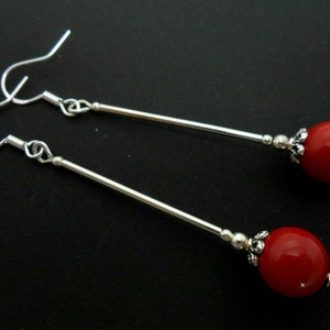 Può includere: Un paio di orecchini pendenti in argento con perline rotonde rosse. Le perline sono attaccate ai montanti in argento con un pezzo decorativo in argento.