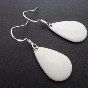 Könnte beinhalten: Ein Paar weiße tropfenförmige Ohrringe mit silbernen Haken.