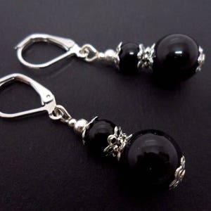 May include: A pair of black onyx earrings with silver hooks and decorative accents. Each earring features two black onyx beads.